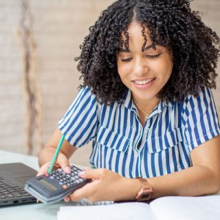 Woman using a calculator, laptop, and notebook.