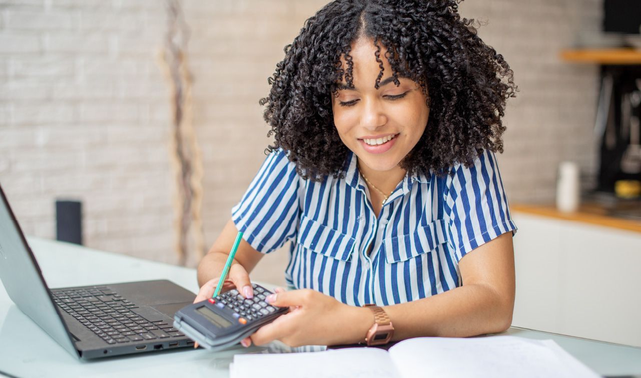 Woman using a calculator, laptop, and notebook.