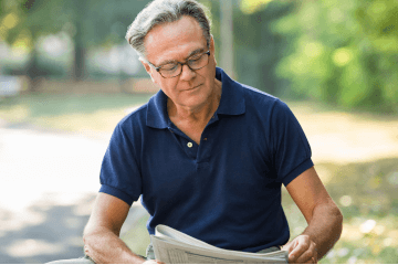 Older man reading a newspaper outside