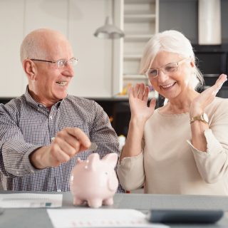 Senior couple putting coin into piggy bank