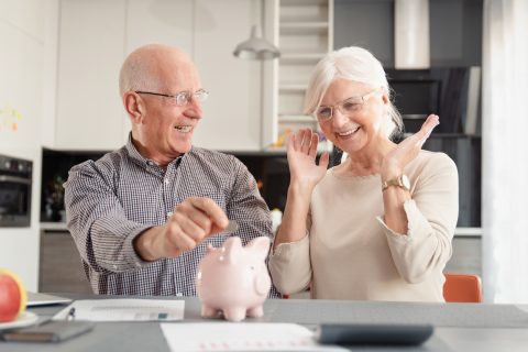 Senior couple putting coin into piggy bank