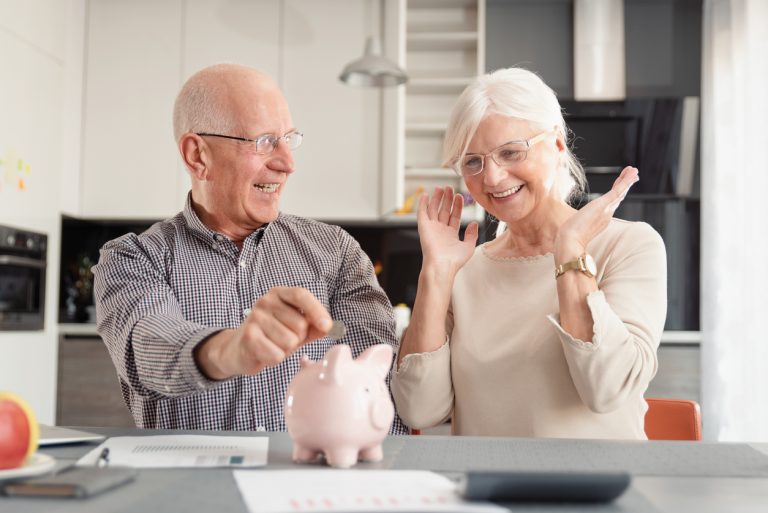 Senior couple putting coin into piggy bank