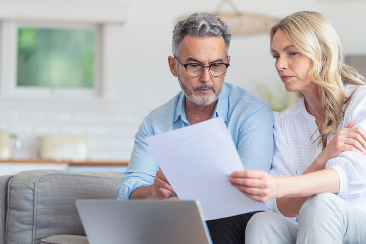 Middle age couple looking at a laptop and paper relating to taxes