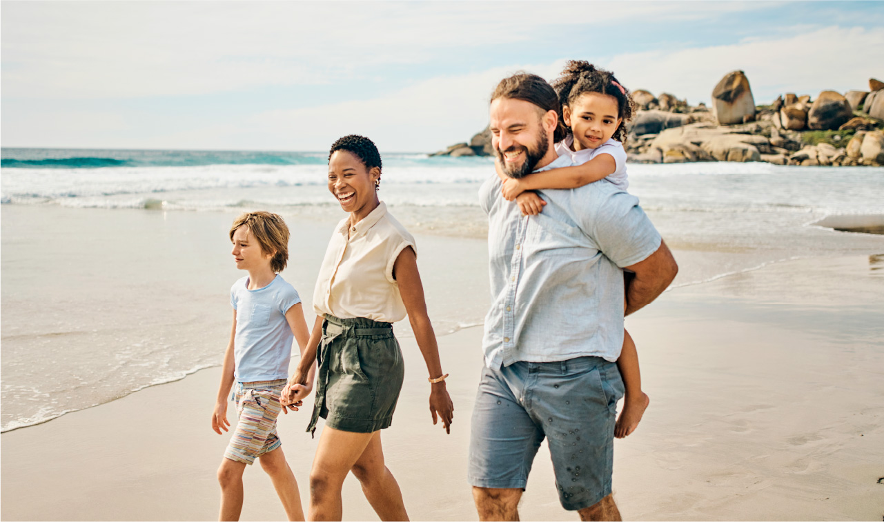 photograph of a smiling family with young children taking a walk on the beach