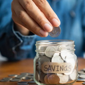 The woman hand is putting a coin in a glass bottle and saving money for future