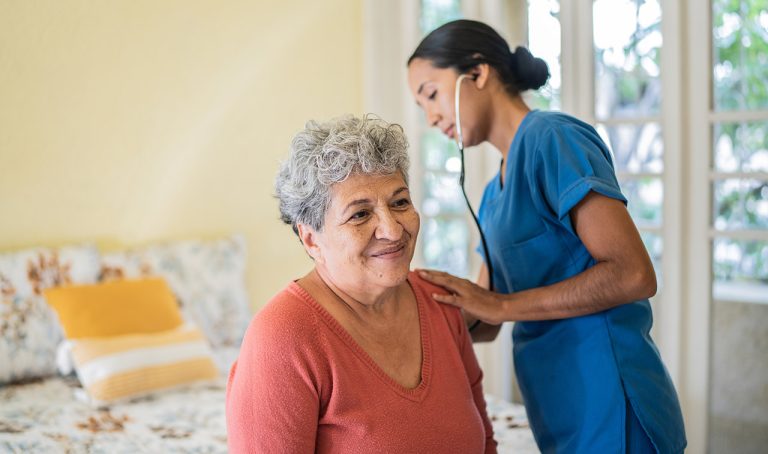 A senior woman receives a check-up from an at-home health aide.