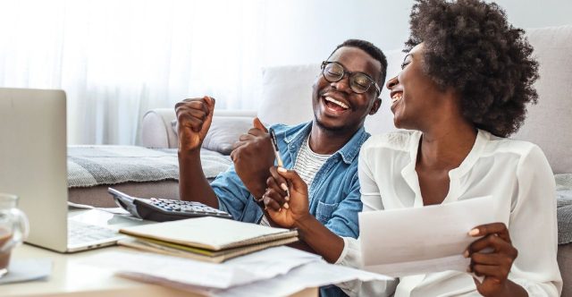 A man and a woman smiling while using a calculator, laptop, and notebook.